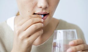 Woman taking a medication pill with a glass of water.