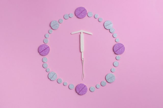 IUD surrounded by birth control pills. IUD vs birth control pill concept.