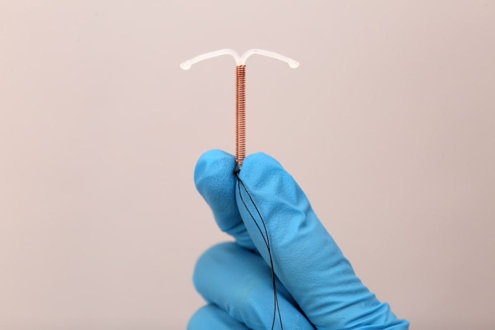 Hand in blue latex glove holding a t-shaped IUD